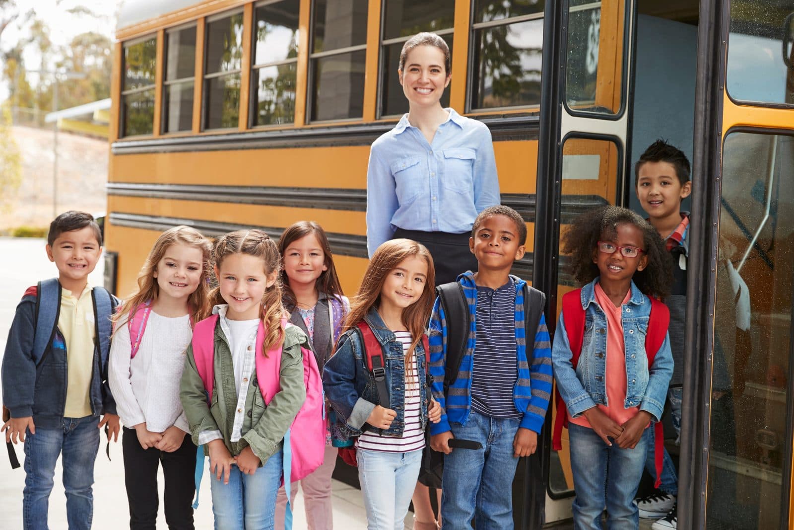 An elementary school teacher and pupils standing beside a school bus