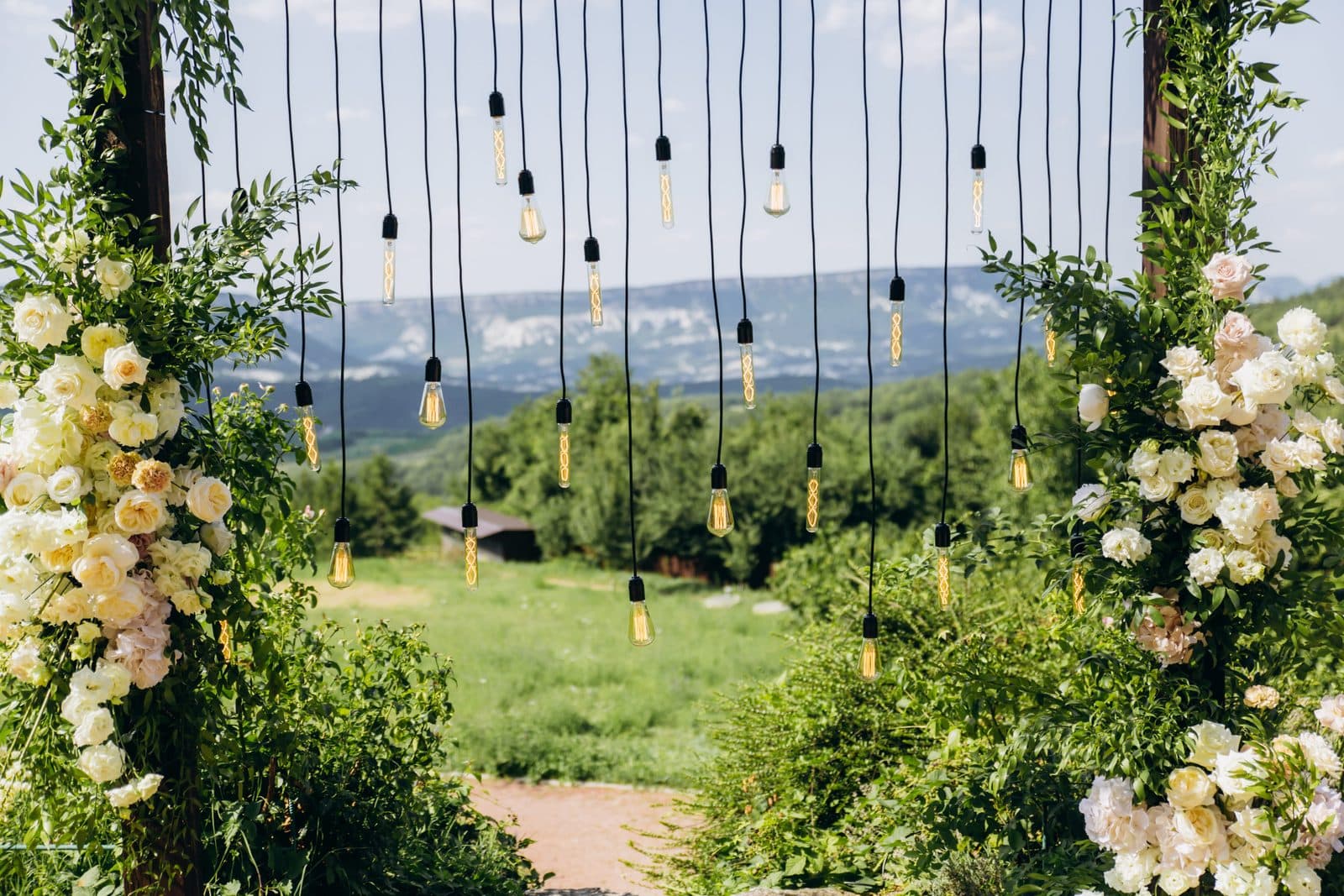 A rustic wedding arch with white flowers and string lights in a park