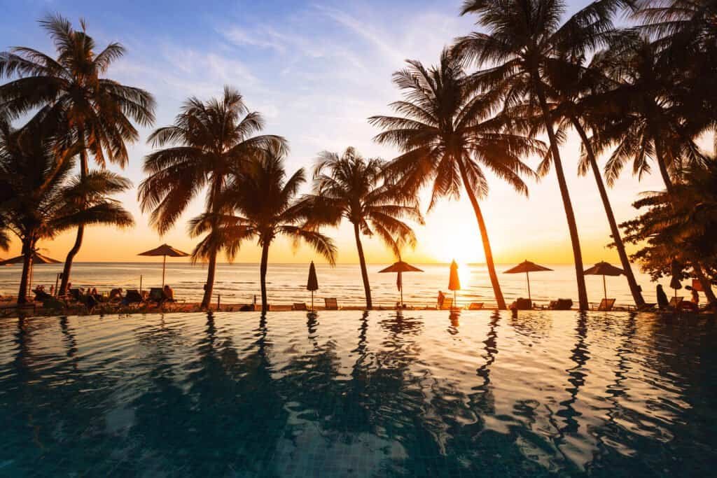 Beautiful sunset on the beach, holidays background, reflection of silhouettes of palm trees in swimming pool of hotel