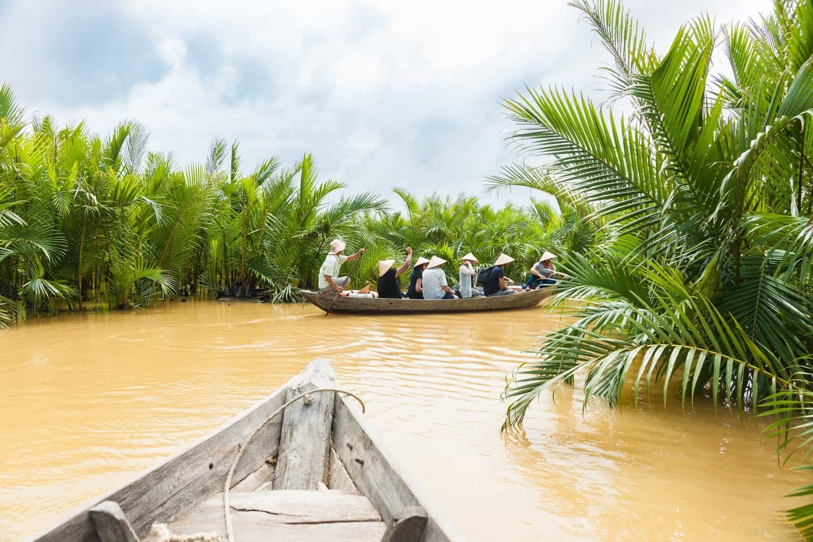 River scene with group of tourists are poled along river between luxuriant palm lined sides in old traditional wooden canoe
