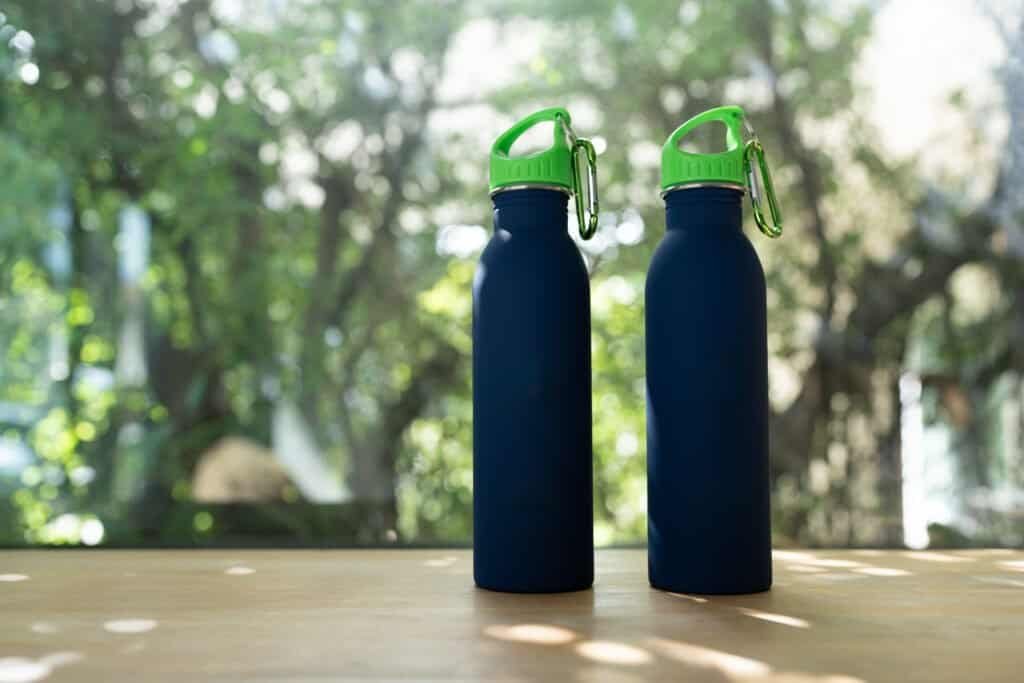 Two blue minimal reusable water bottle is sitting on a wood table with natural sunlight