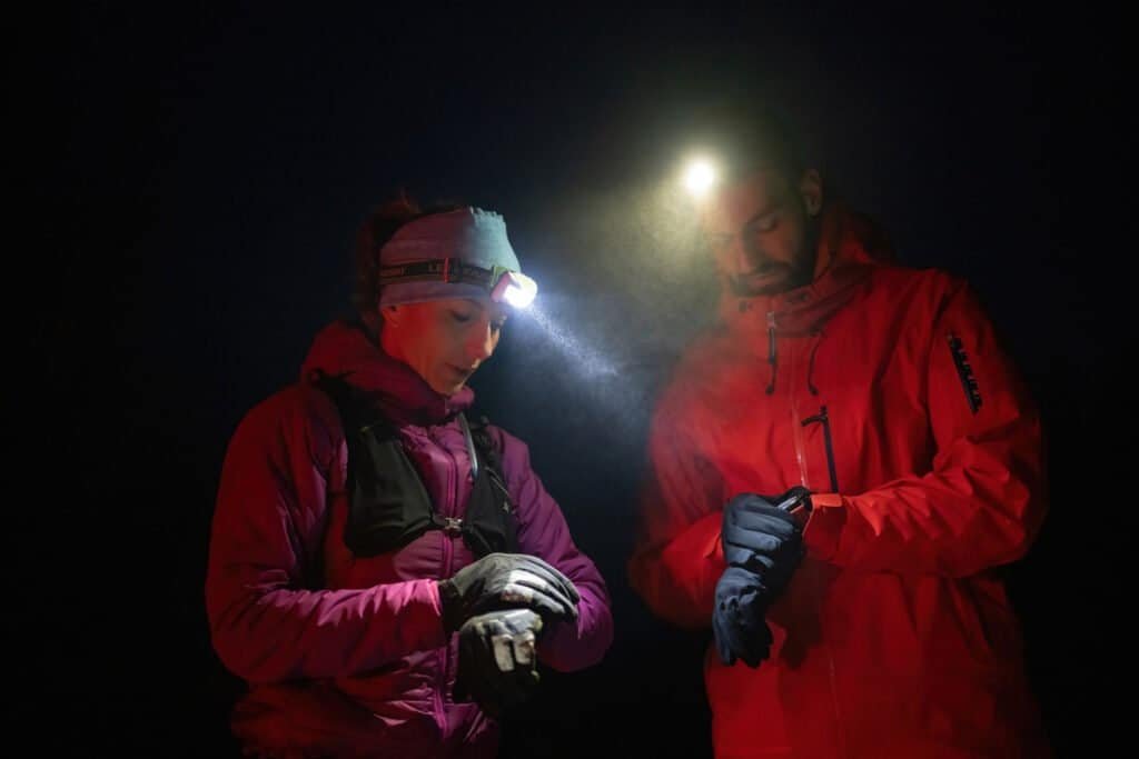 Couple night hikers examine a device under headlamp light, emphasizing navigation and teamwork under low light conditions.