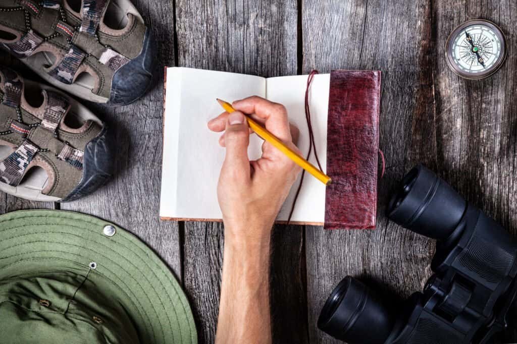 Man writing in the notebook on the wooden table with traveler outfit