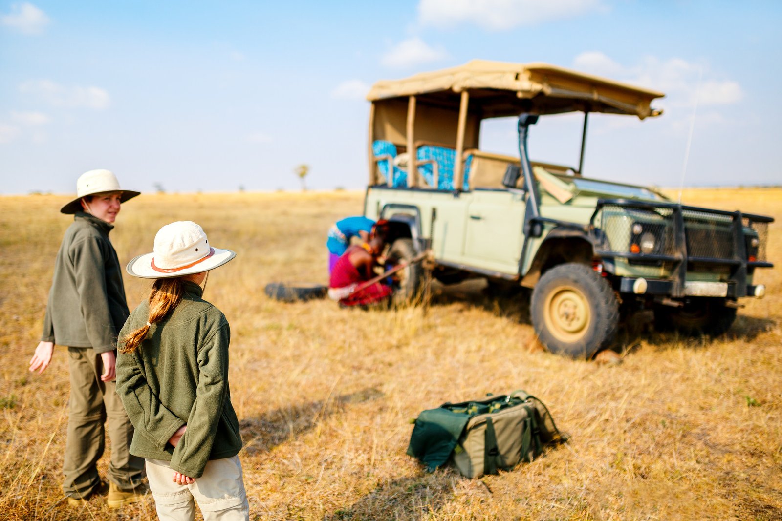 Kids in kenya safari on morning game drive in open vehicle looking at maasai guides